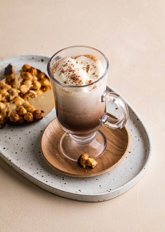 Glas mit Irish Coffee, bedeckt mit Schlagsahne und Kakaopulver, auf einem ovalen Teller mit Walnüssen
