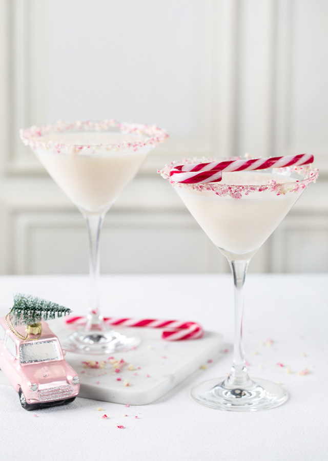 Zwei Martini-Gläser mit weißem Getränk und Zuckerrand, daneben ein Miniaturauto mit kleinem Weihnachtsbaum und zwei Zuckerstangen