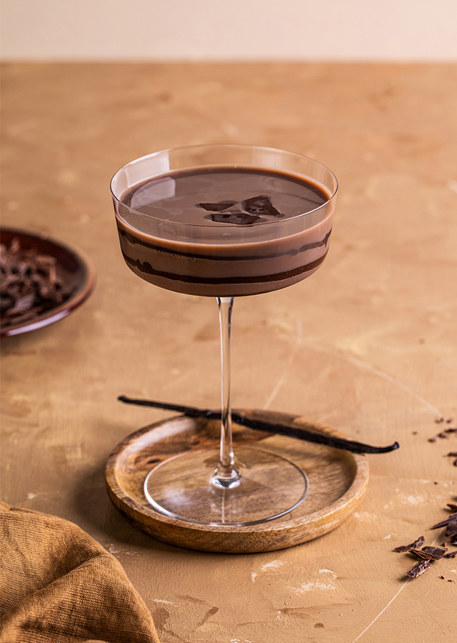 Cocktailglas mit Schokoladencreme-Martini auf einem Untersetzer umgeben von Schokoladenraspeln und Vanilleschote