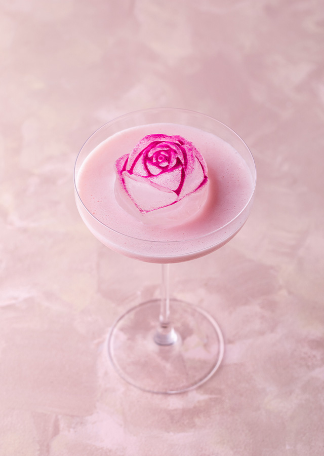 Cocktailglas mit rosa Schaum und einer essbaren Rose als Dekoration