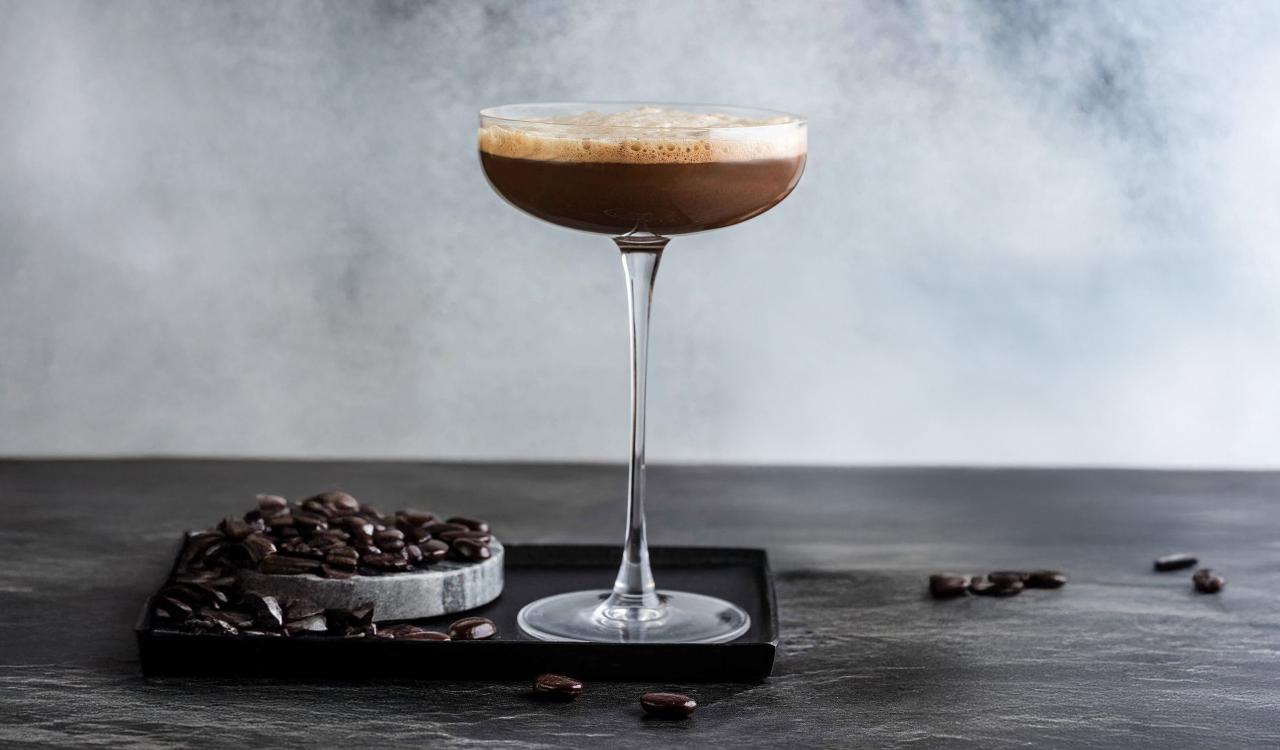 Cocktailglas mit Espresso-Martini auf dunklem Untergrund neben Kaffeebohnen und Schokoladenstücken