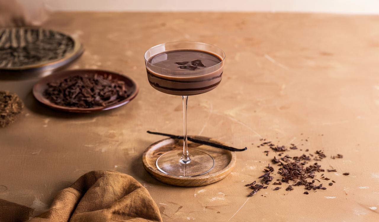 Cocktailglas mit Schokoladencreme-Martini auf einem Untersetzer umgeben von Schokoladenraspeln und Vanilleschote
