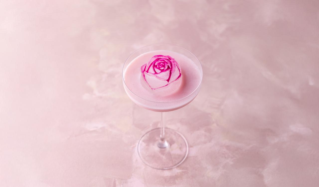 Cocktailglas mit rosa Schaum und einer essbaren Rose als Dekoration